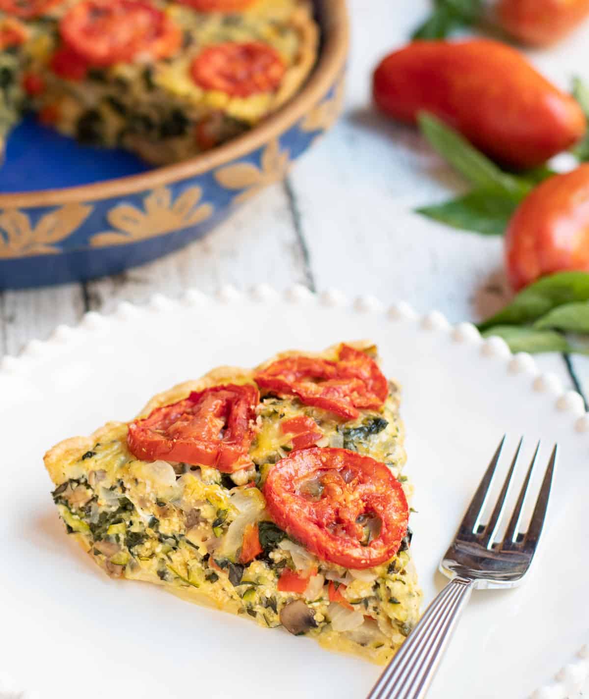 Slice of Mushroom, Spinach, Tomato and Zucchini Pie on a white plate