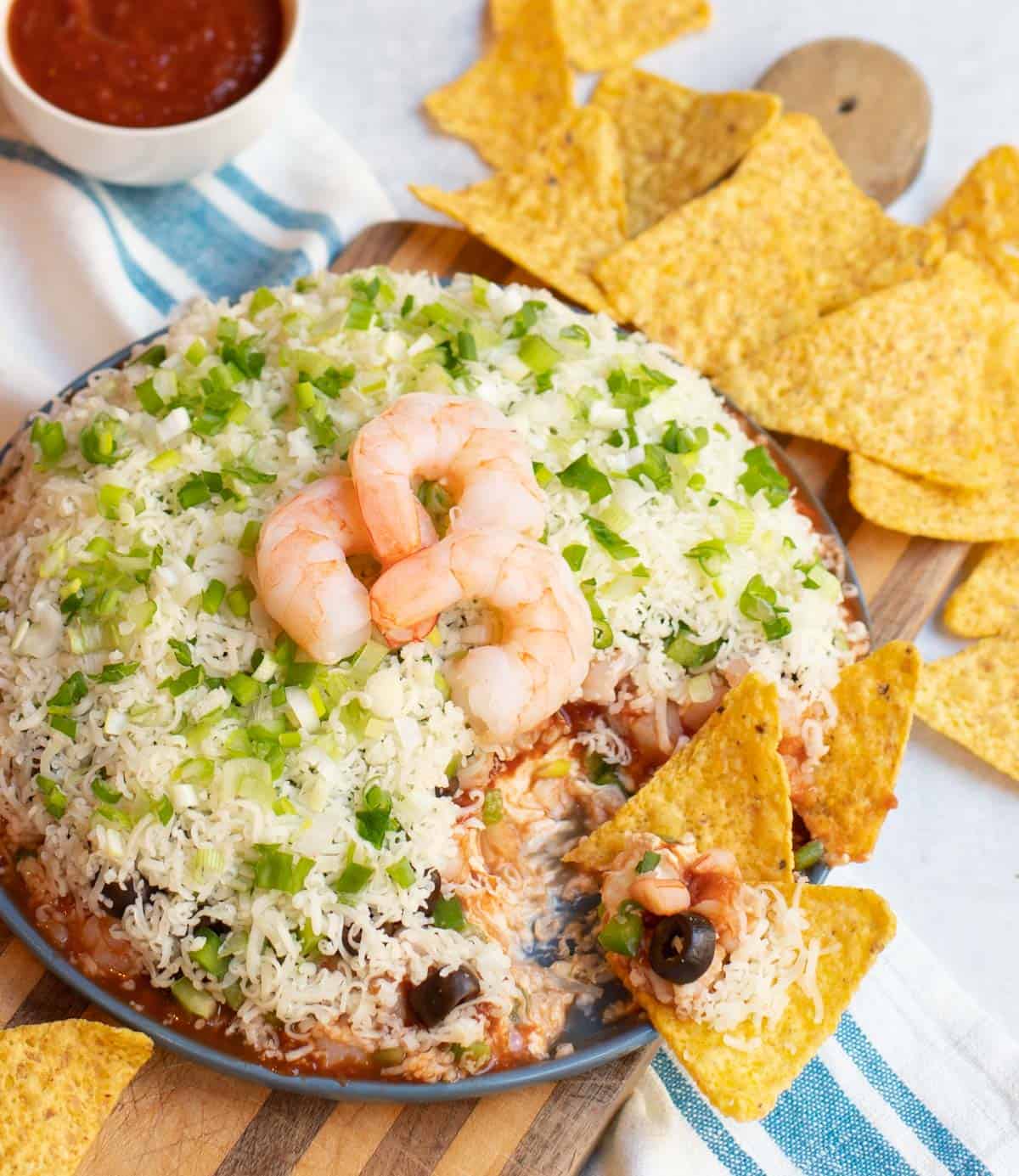 Layered Shrimp Cocktail Dip with tortilla chips on a blue plate