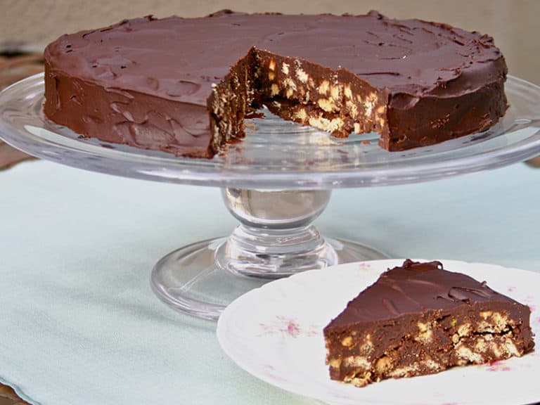 Biscuit cake sitting on a glass cake stand with one piece cut out and sitting on a plate in front