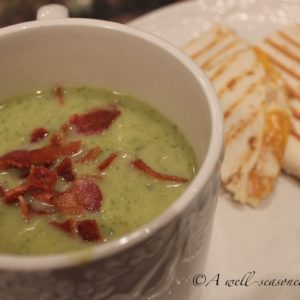 Large white mug filled with a single portion of Zucchini Soup, on a plate next to a panini sandwich.