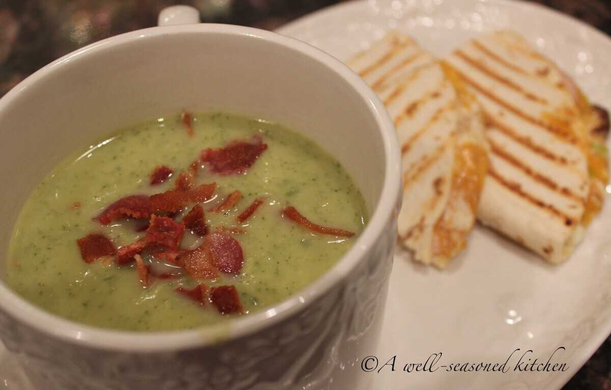 Large white mug filled with a single portion of Zucchini Soup, on a plate next to a panini sandwich.