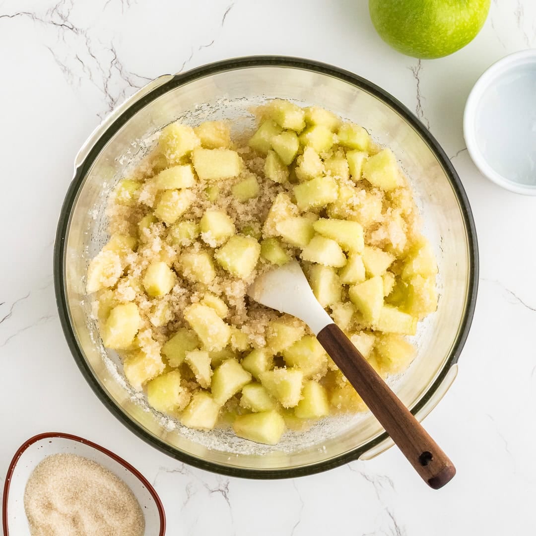 Diced apples in a mixing bowl with sugar added.