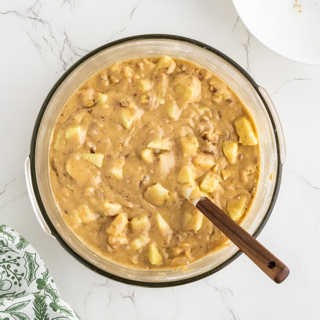 Apple cake batter in a bowl with a spatula in the bowl.