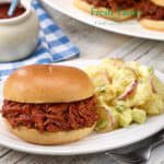 white plate with a single serving of Dorothy's Potato Salad next to a BBQ Beef sandwich.
