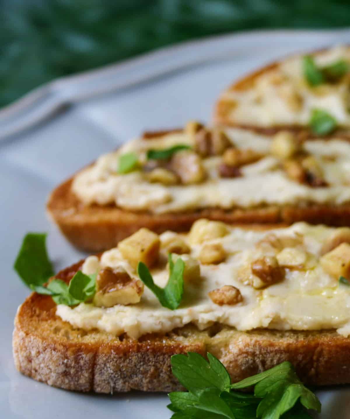 portions of 3 bruschetta topped with cannellini bean puree and walnuts, on a blue plate