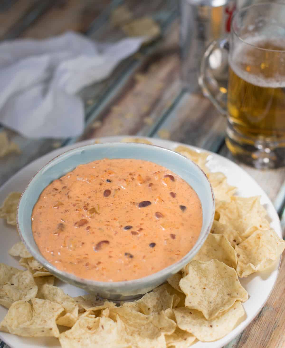 Chili Cheese Dip in a blue bowl with chips on a plate
