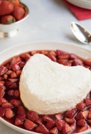 heart shaped coeur a la creme with a spoon inserted in the side, and surrounded by strawberry sauce