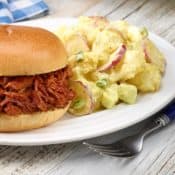 white plate with Dorothy's Potato Salad next to BBQ Beef sandwich