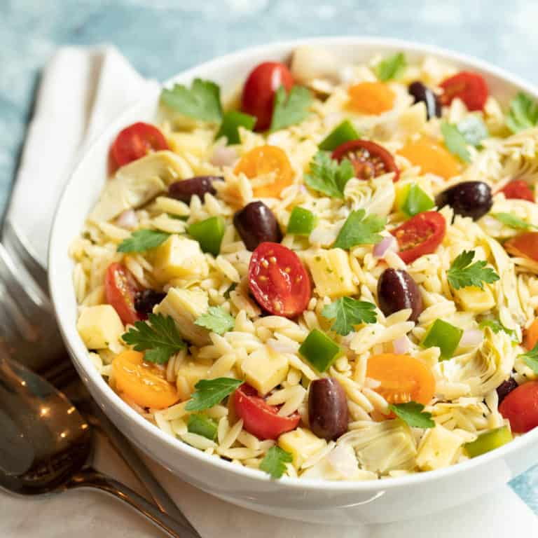 White bowl filled with Greek Orzo Pasta; Lemon-Basil Tahini Dressing is in a glass pitcher on the side