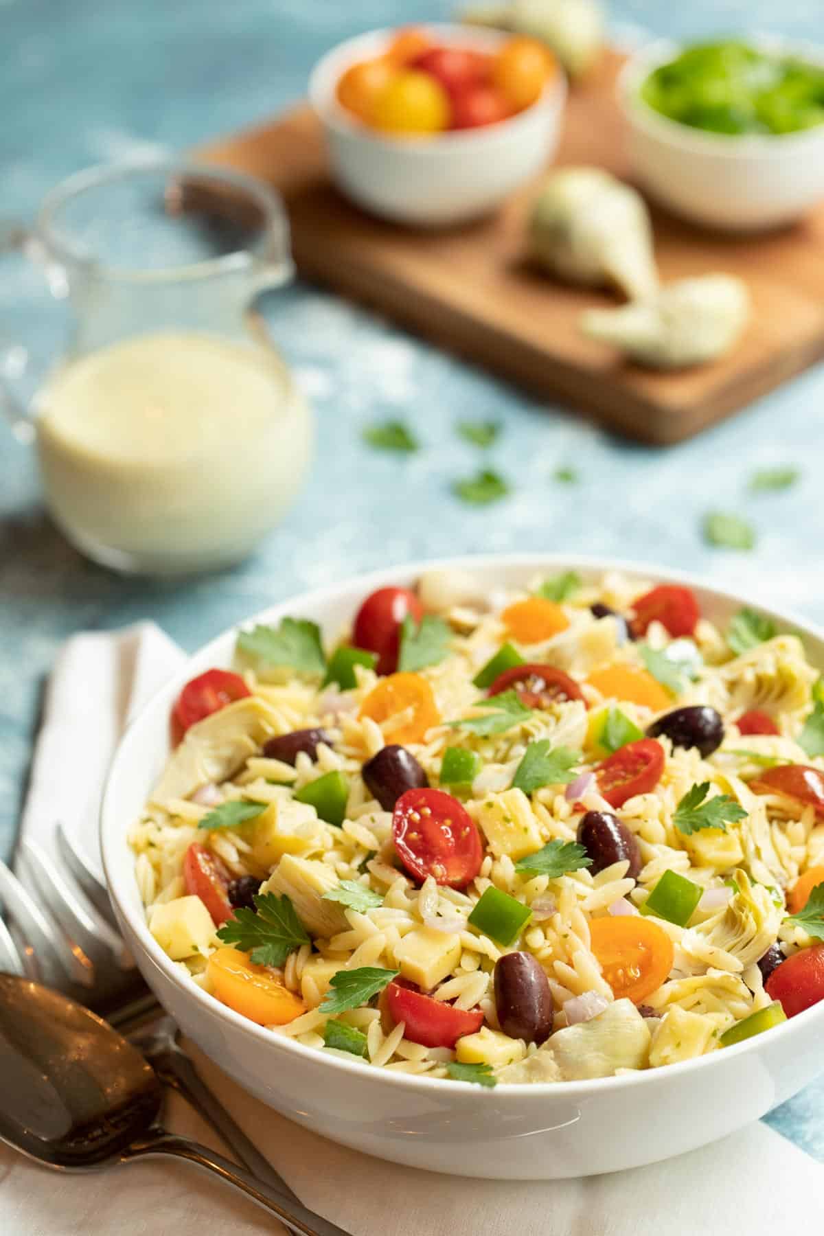 White bowl filled with Greek Orzo Salad with Lemon-Basil Tahini Dressing. Dressing is on the side