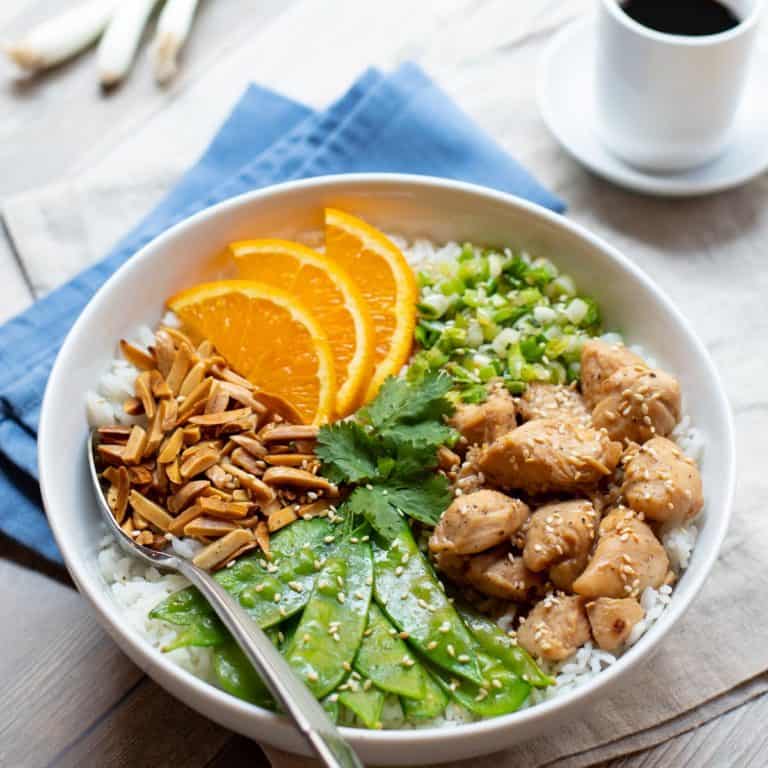 stir fry chicken, pea pods, almonds, green onion and rice arranged in a flat bowl