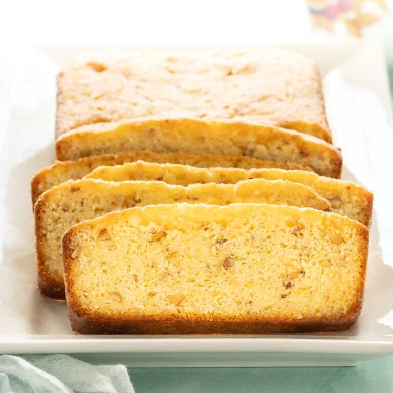 several slices of lemon bread stacked vertically, with the rest of the lemon loaf behind