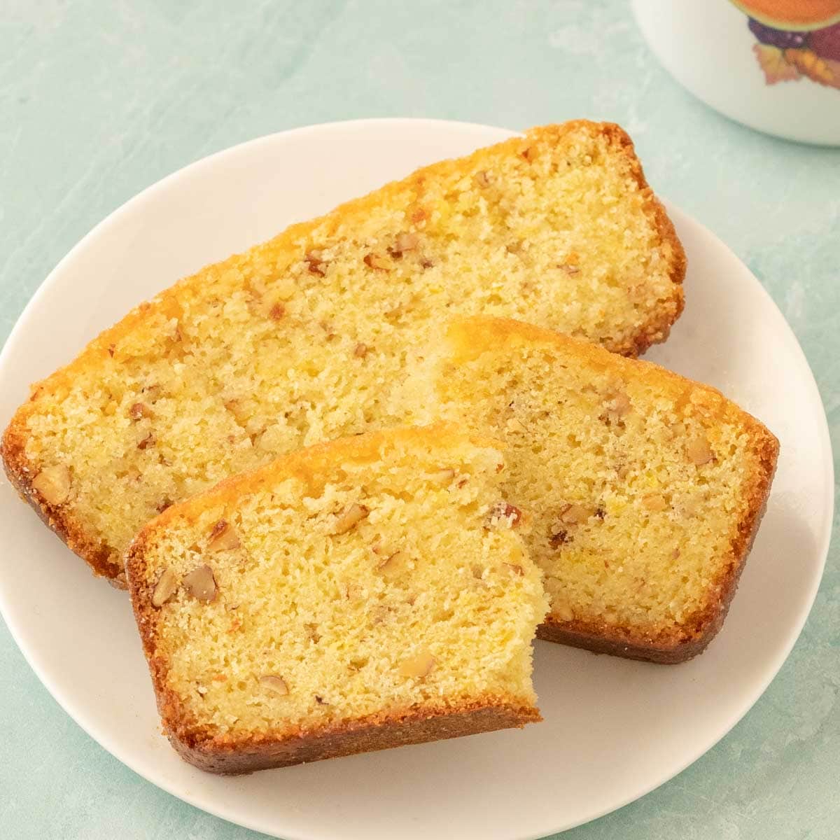 Two slices of lemon bread on a white plate, the top one broken in half