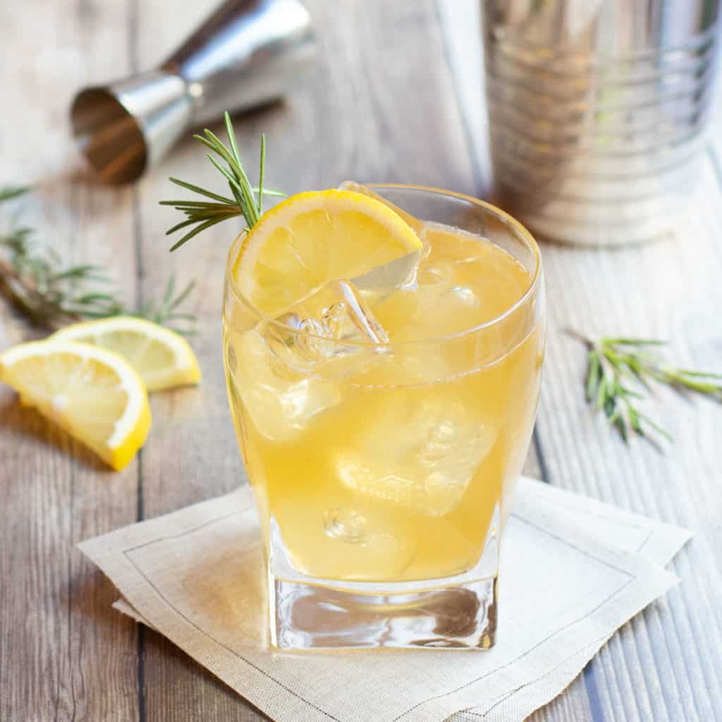 lemon ginger bourbon cocktail over ice in a glass, garnished with a lemon slice