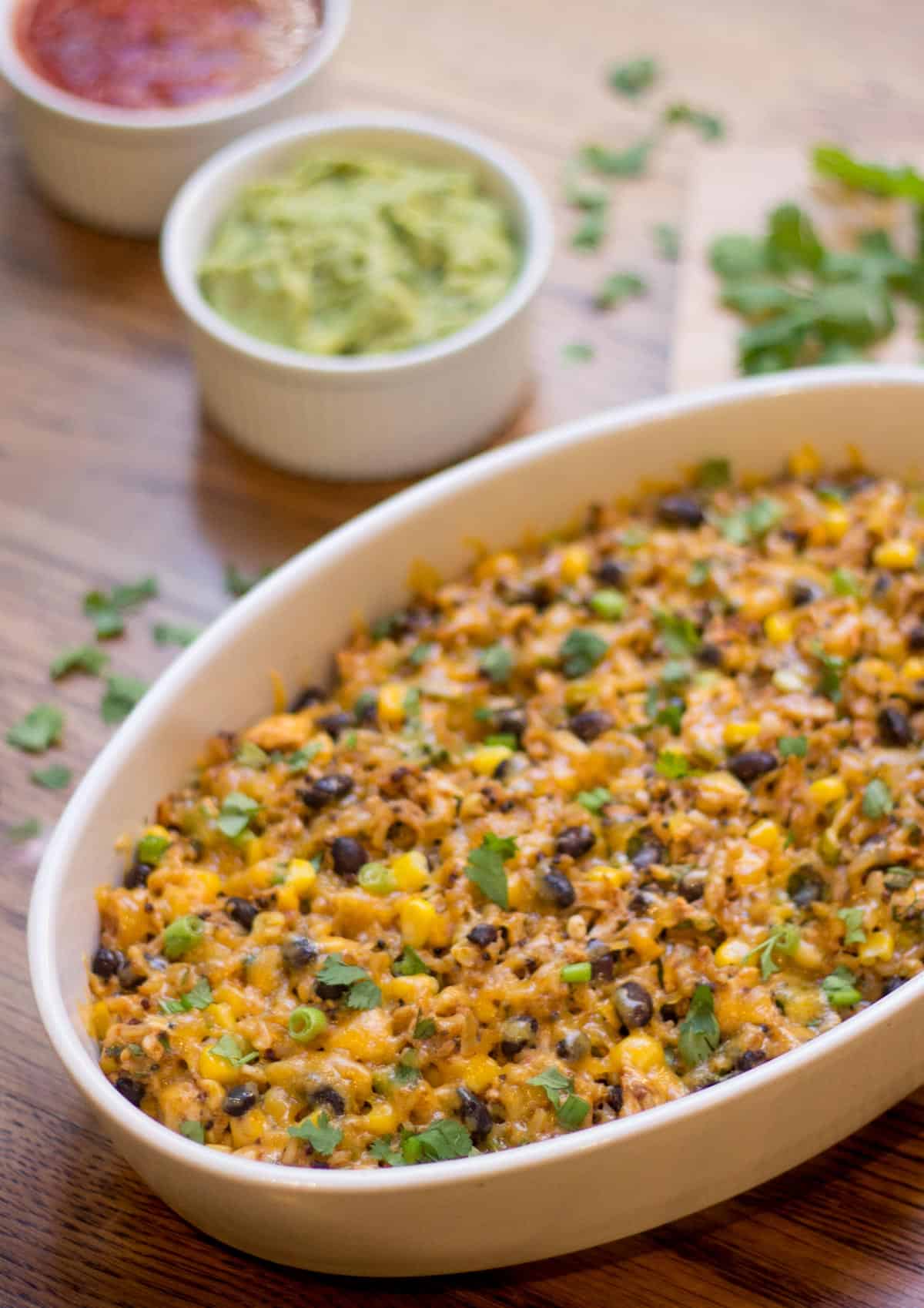 Casserole dish holding Mexican chicken, black beans and rice, with guacamole and salsa on the side