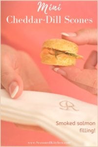 Image is formatted for pinning onto pinterest. A hand is holding a Mini Cheddar Dill Scone with a napkin underneath