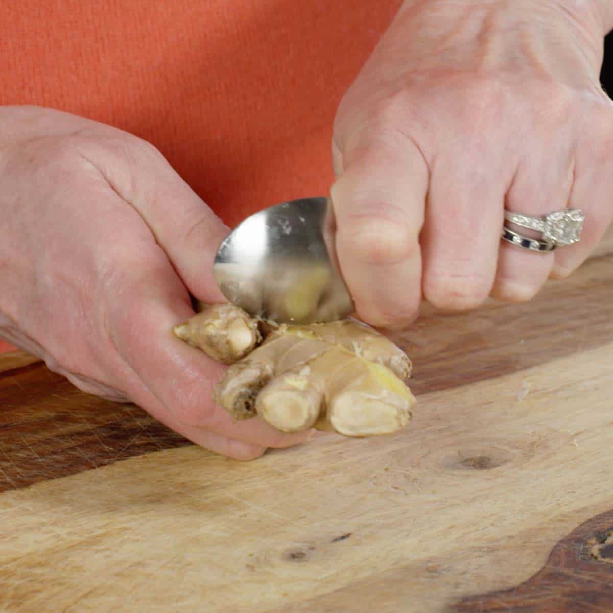 hands using a tablespoon to peel fresh ginger