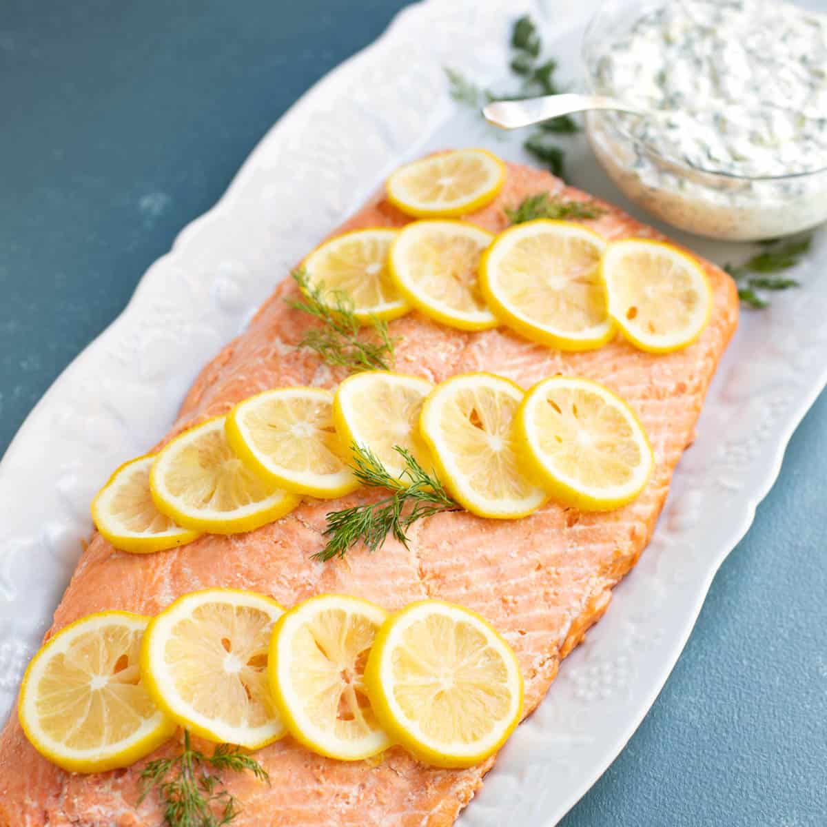 Poached salmon garnished with lemon slice and dill, with a side of cucumber dill sauce