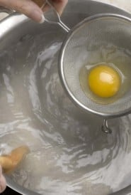 raw egg in a strainer over boiling water, getting ready to poach the egg