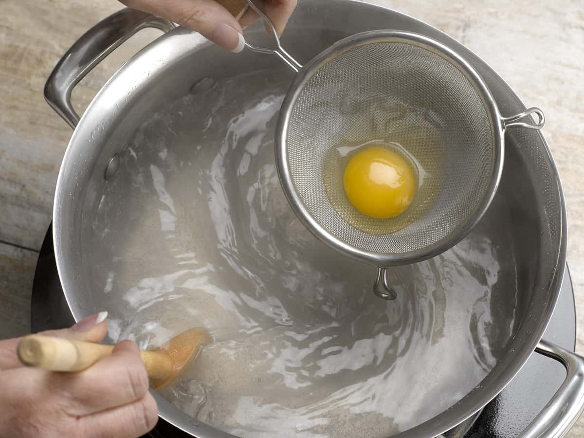 raw egg in a strainer over boiling water, getting ready to poach the egg