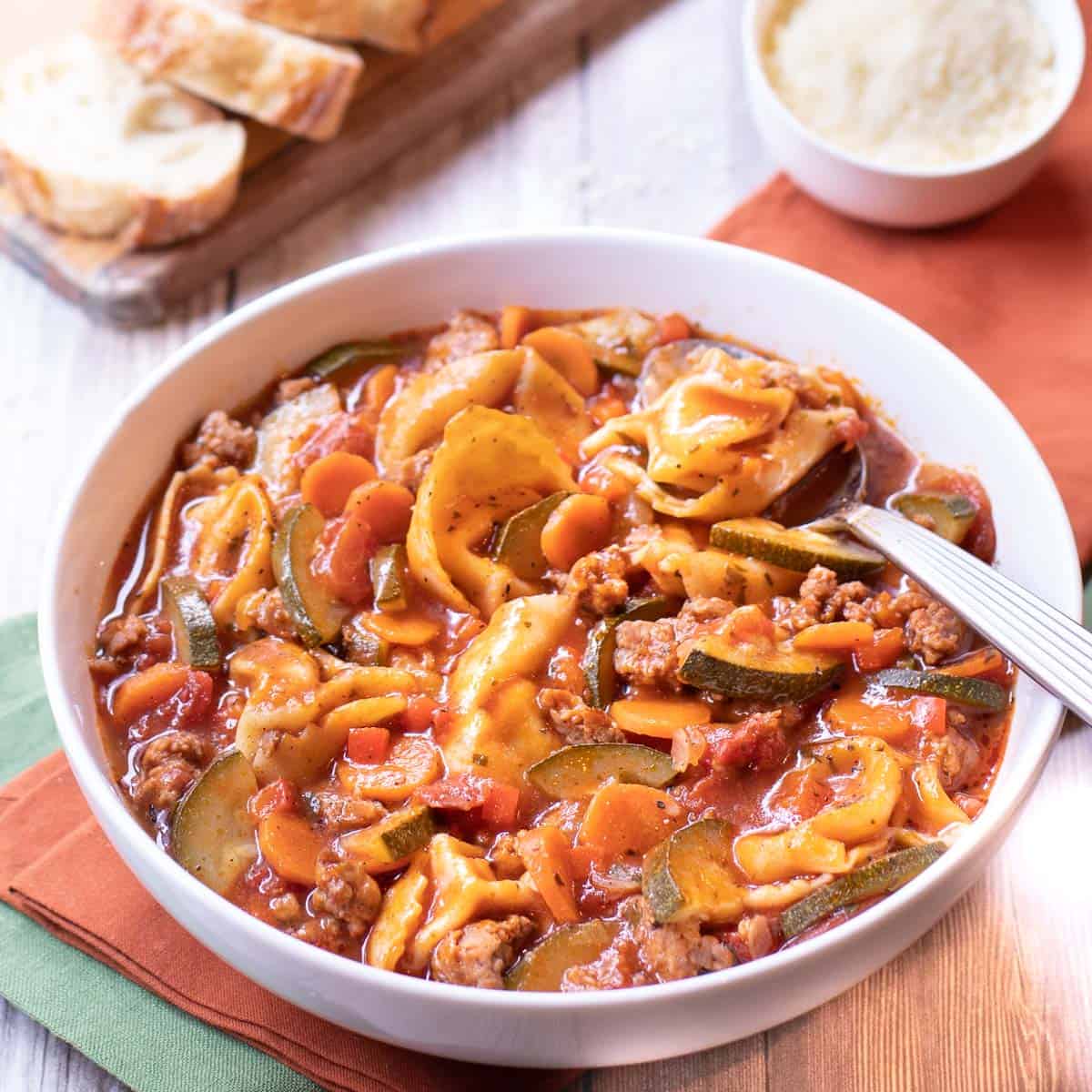 Bowl of soup with tortelloni, sausage, zucchini and carrots.