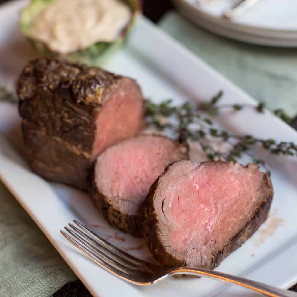 whole roasted beef tenderloin with a few slices in front and sauce on the side