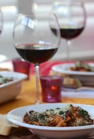 White bowl filled with Spinach Farfalle Bolognese, sitting with a glass of red wine