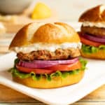 White platter with Sundried Tomato Turkey Burger and Lemon-Green Onion Sauce on a pretzel bun