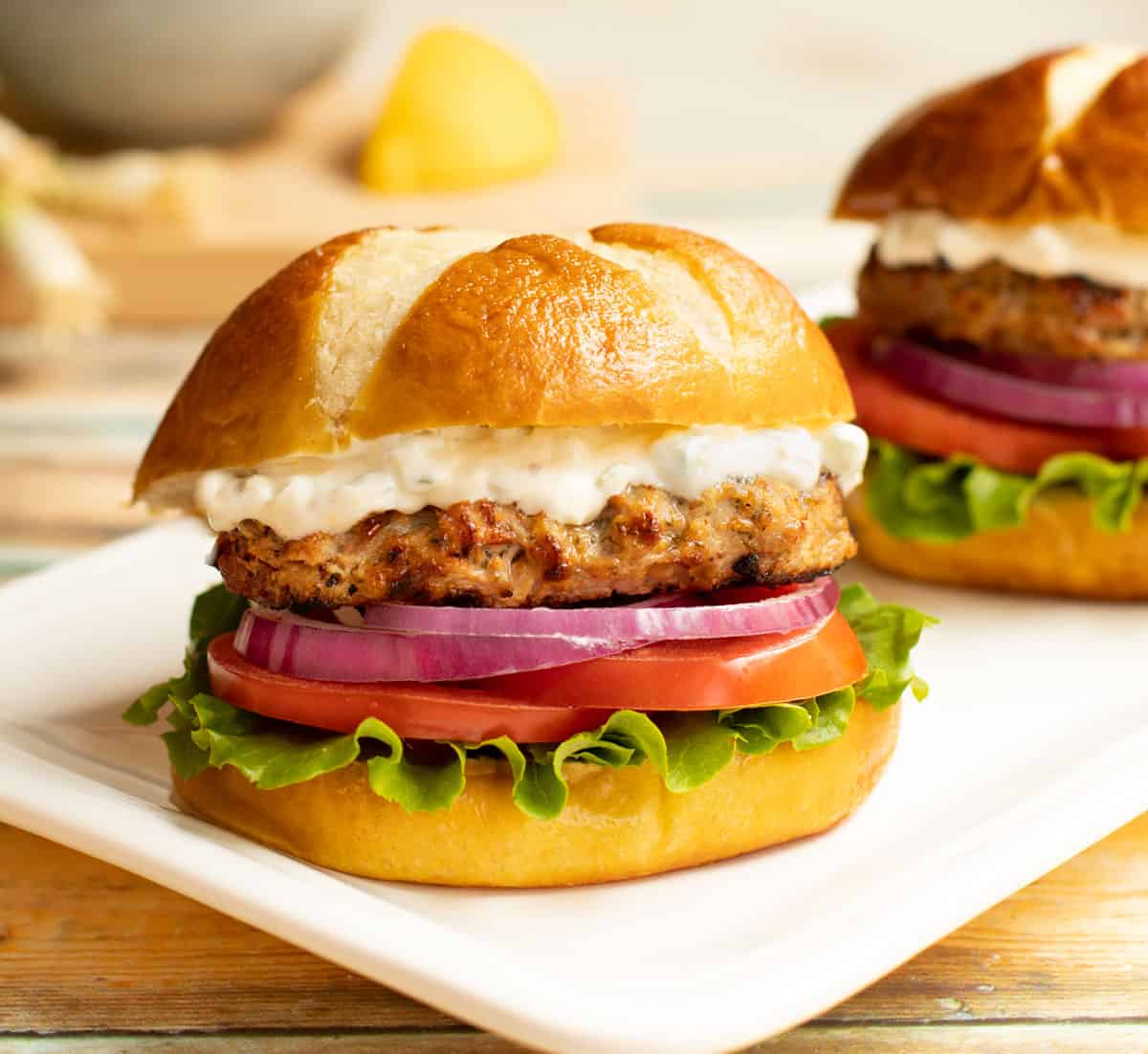 White platter with Sundried Tomato Turkey Burger and Lemon-Green Onion Sauce on a pretzel bun