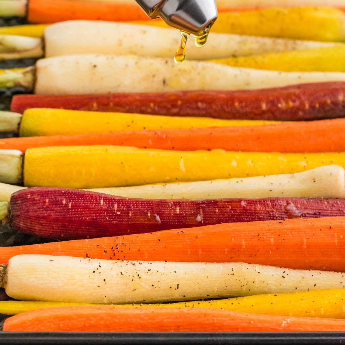 Drizzling oil over carrots on a baking pan.