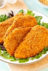 4 Air Fryer Fried Chicken Breasts on a plate, with fresh lettuce around the edges