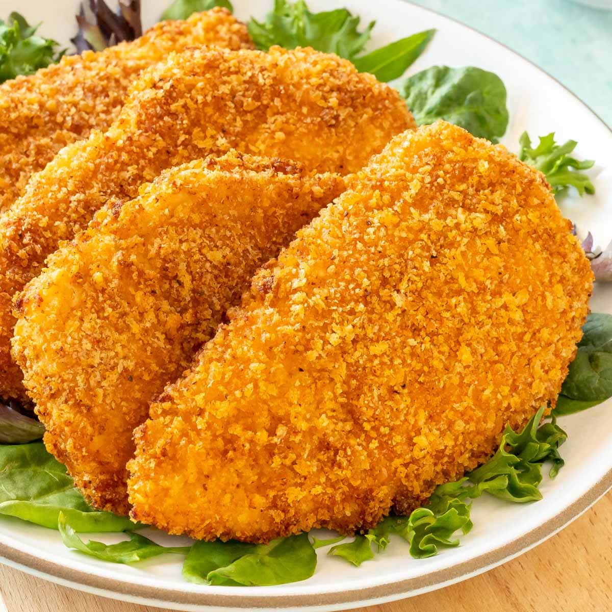 CLose up of 4 Air Fryer Fried Chicken Breasts on a plate, with fresh lettuce around the edges