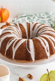 Apple bundt cake on a cake stand drizzled with glaze.