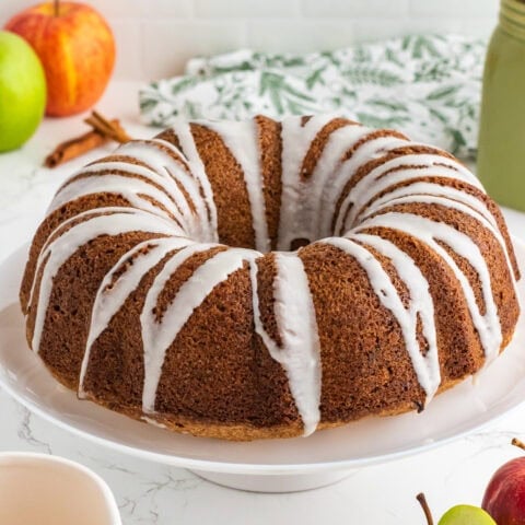 Apple bundt cake on a cake stand drizzled with glaze.