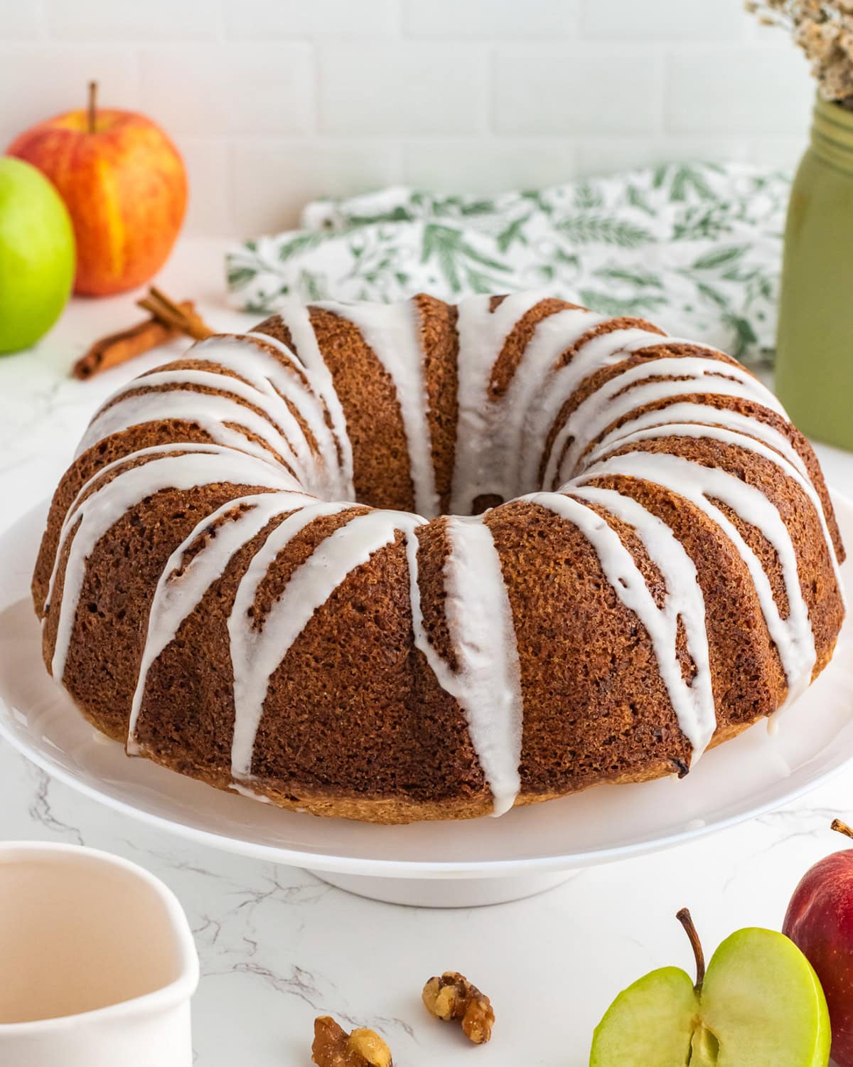 Apple bundt cake on a cake stand drizzled with glaze.