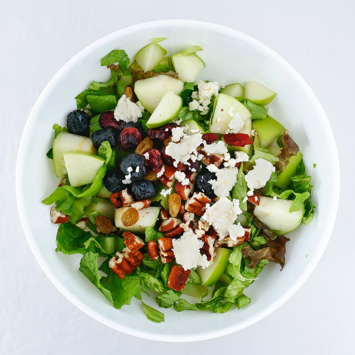 Apple salad with feta ingredients added to a white bowl.