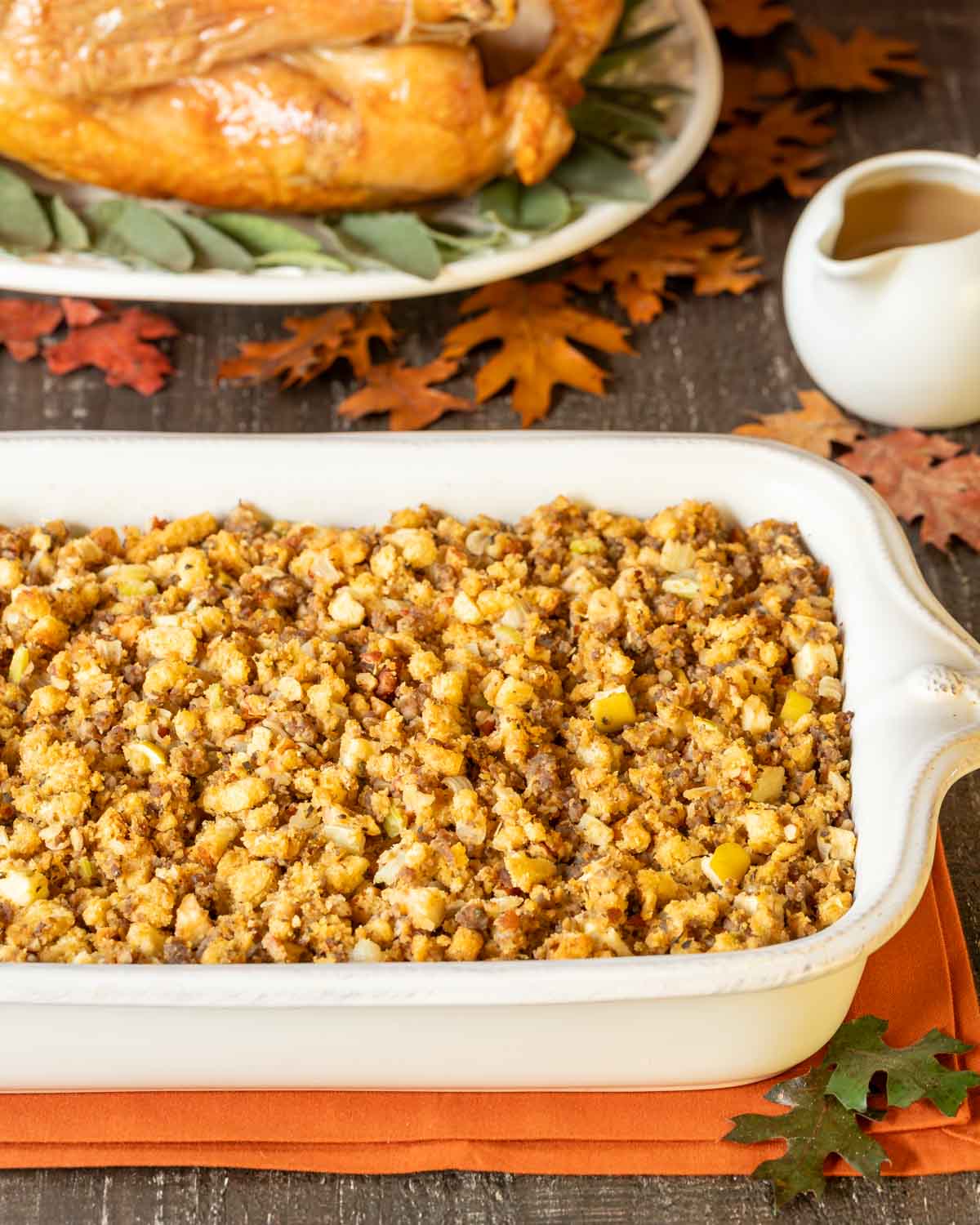 White baking dish holding Apple Sausage Stuffing with a roast turkey and gravy in the background