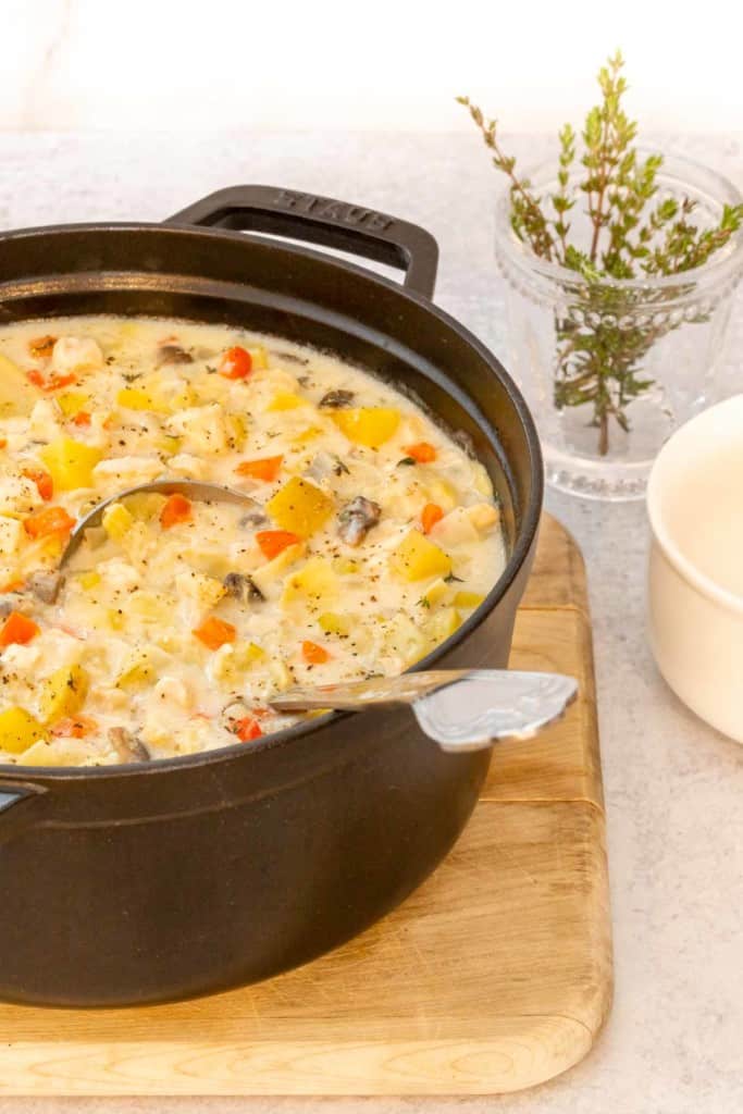 Black stock pot filled with Creamy Artichoke Chicken Soup, with a small bowl alongside
