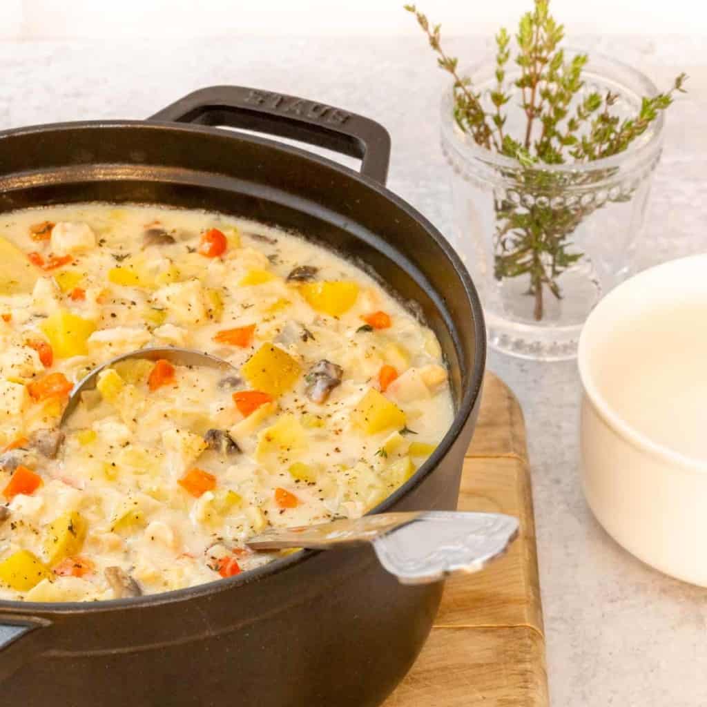 Large black stock pot holding Creamy Artichoke Chicken Chowder, with a bowl and fresh thyme alongside