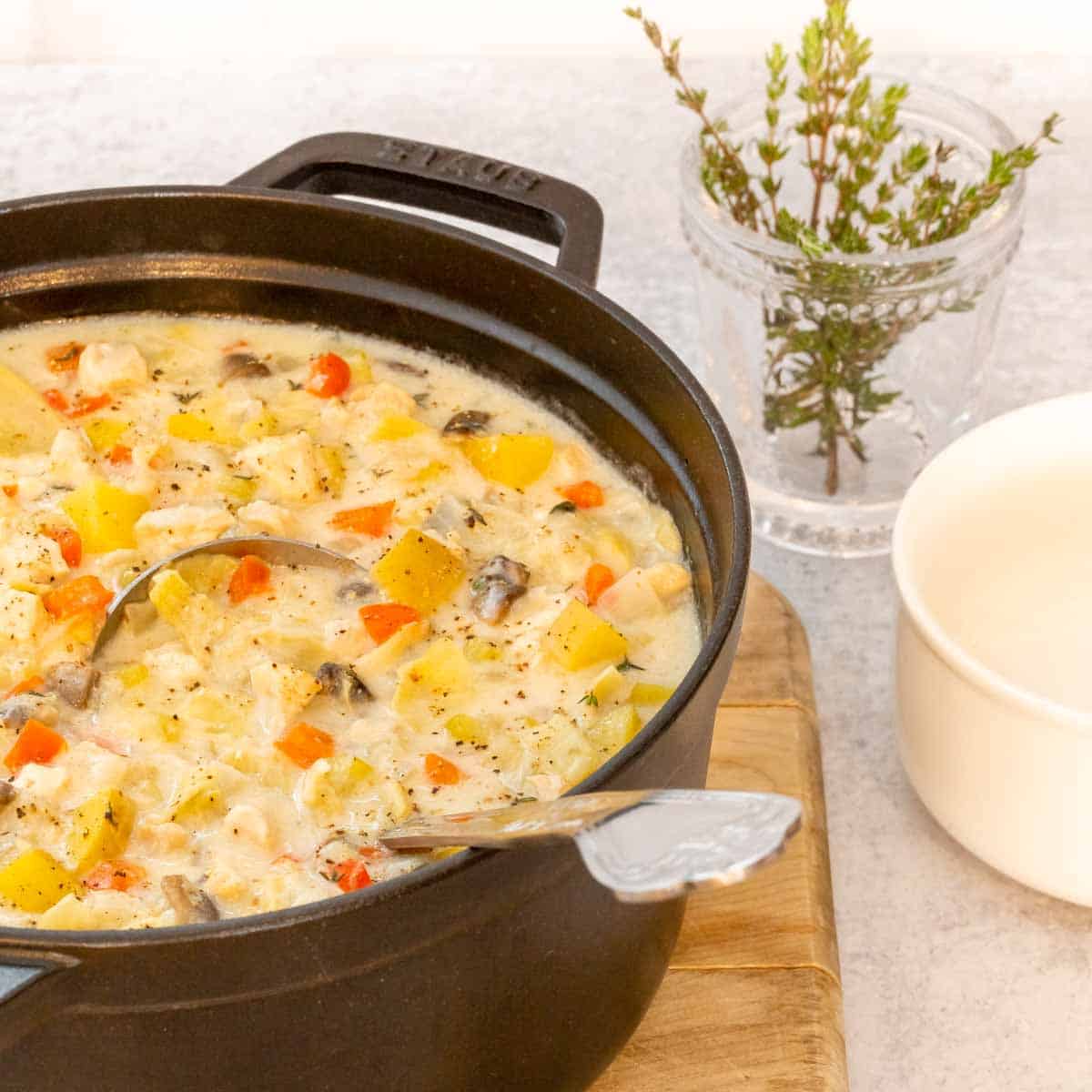 Large black stock pot holding Creamy Artichoke Chicken Chowder, with a bowl and fresh thyme alongside.