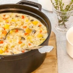 Large black stock pot holding Creamy Artichoke Chicken Chowder, with a bowl and fresh thyme alongside