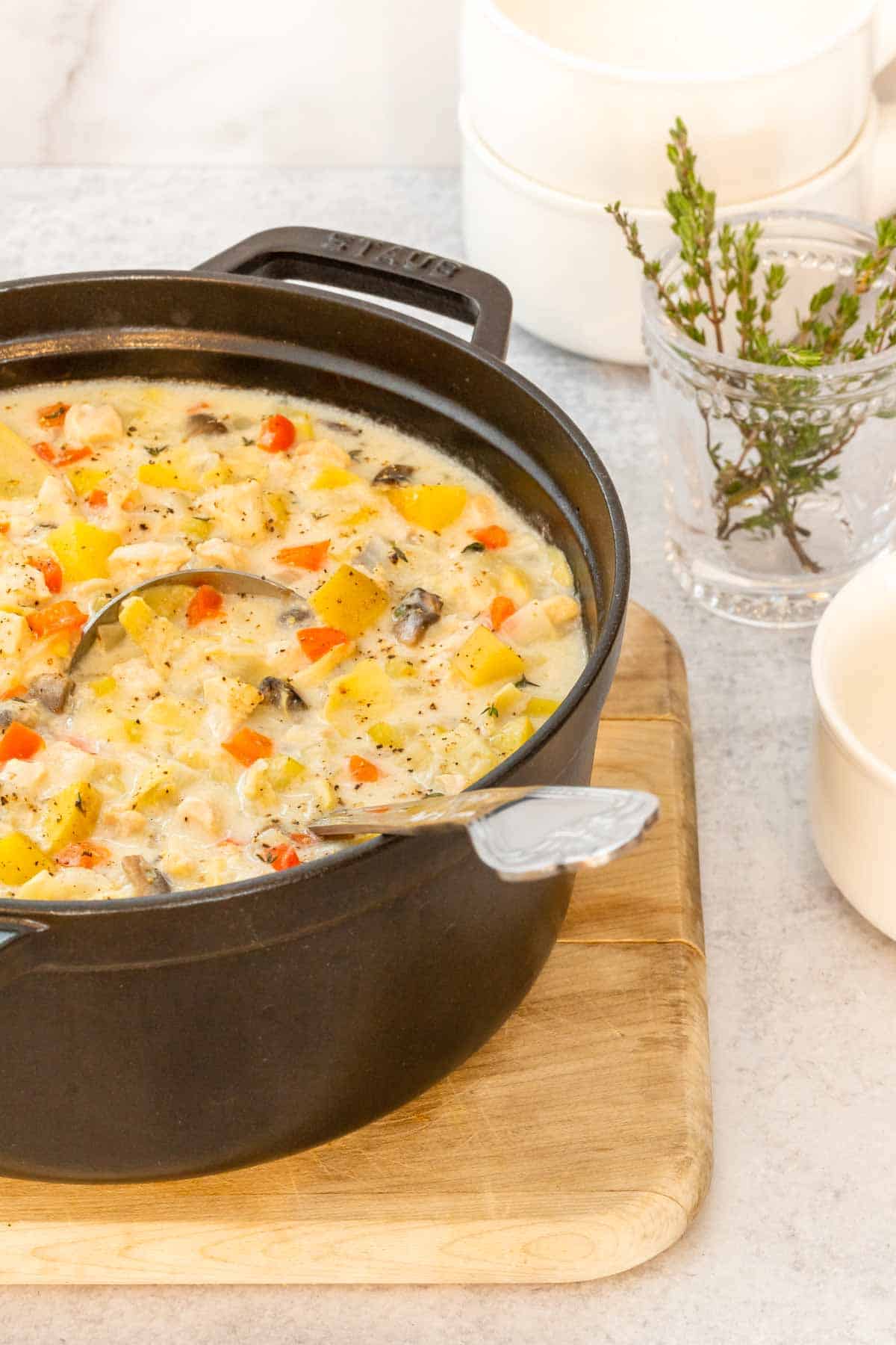 Large black stock pot holding Creamy Artichoke Chicken Chowder, with a bowl and fresh thyme alongside