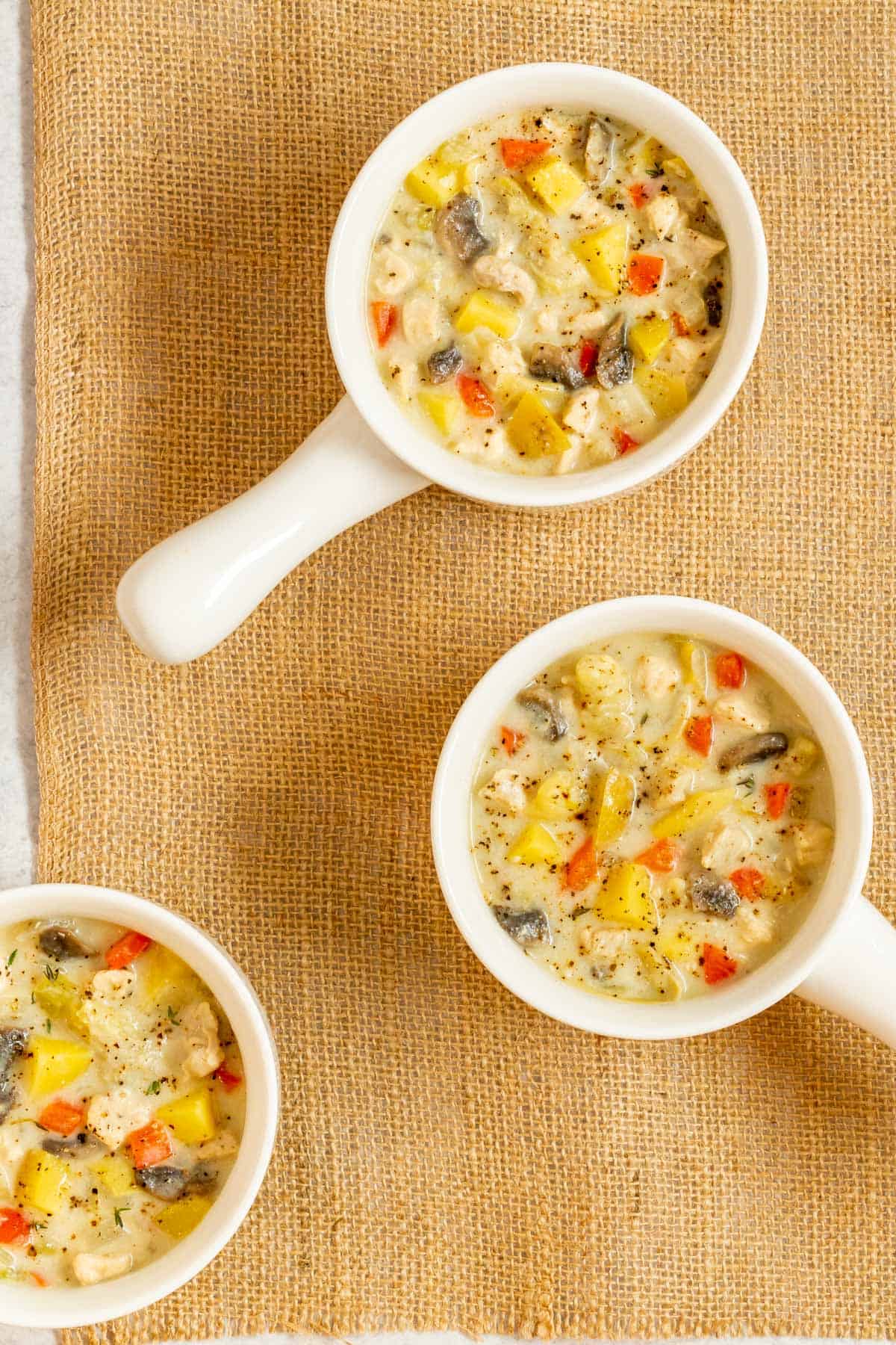 overhead view of 3 white bowls holding individual servings of Creamy Artichoke Chicken Chowdder