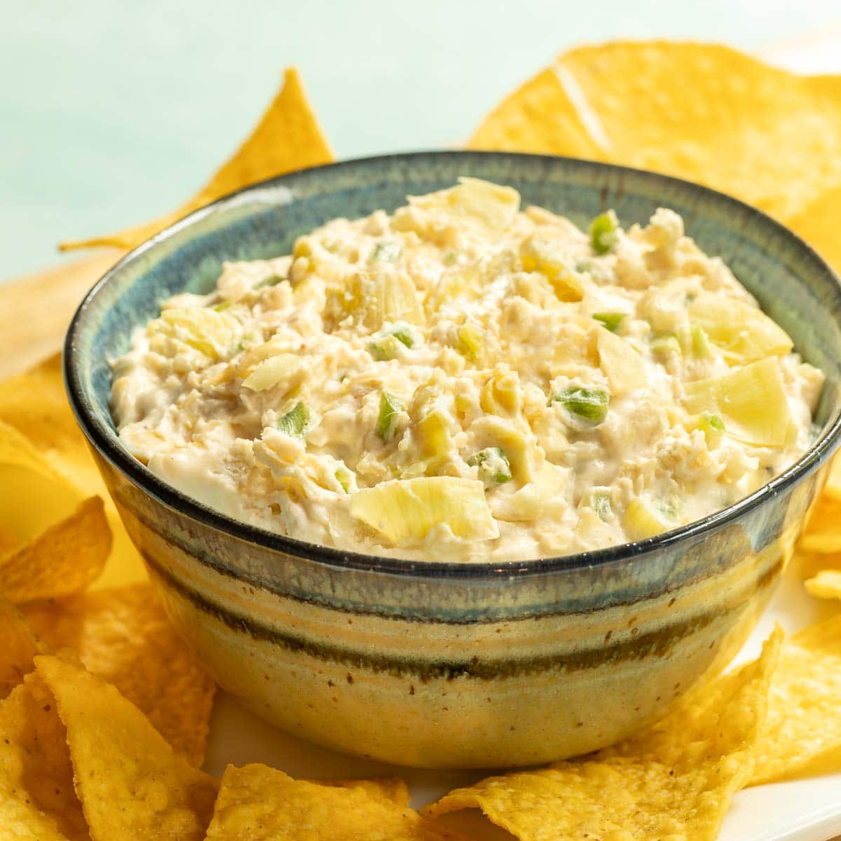 Blue striped bowl holding Jalapeno Artichoke Dip, surrounded by tortilla chips