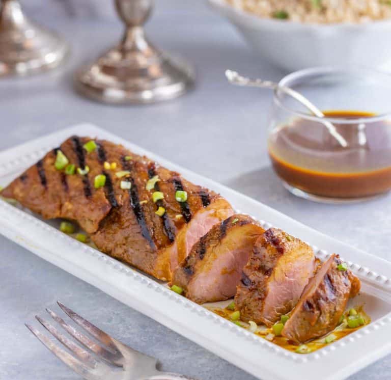 white platter filled with slices of Asian Pork Tenderloin. Bowl if rice and candles in the background