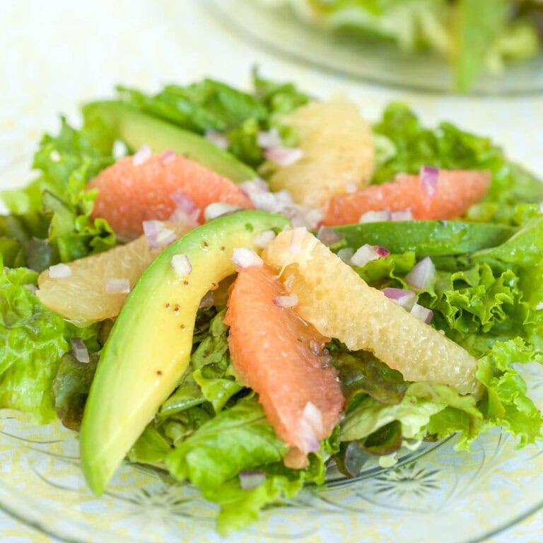 Individual serving of Avocado Grapefruit Salad with slices of avocado, pink, and white grapefruit alternating in a pinwheel on greens