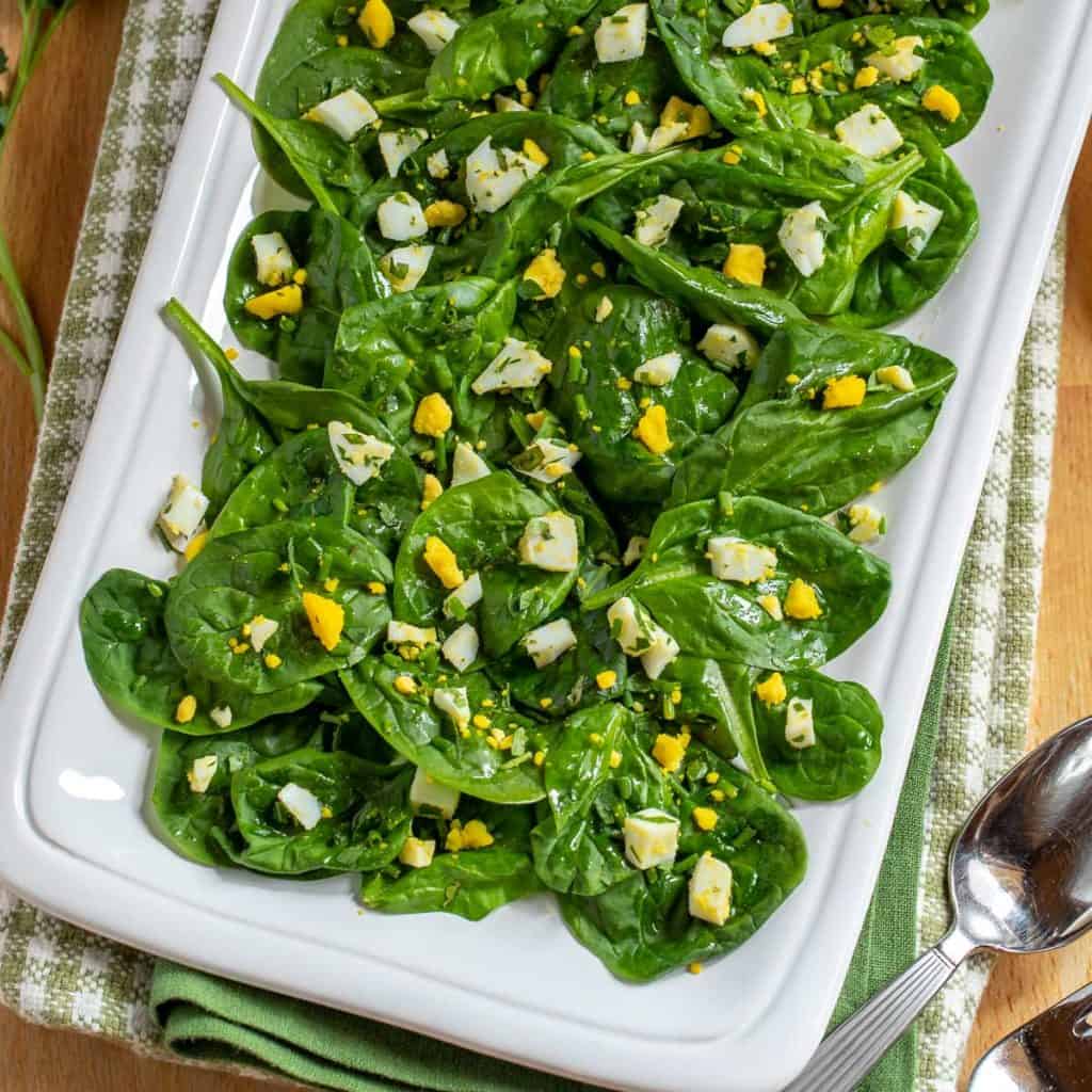 Close up of white square platter showing Baby Spinach Salad with Lemon Dijon Dressing