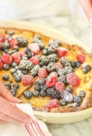 Oval baking dish filled with Baked Cinnamon French Toast, topped with berries and a spoon dishing out one serving