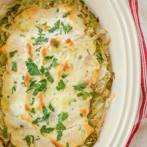 Overhead of white dish holding Baked Fish topped with a mayo sauce and sitting on shredded lettuce