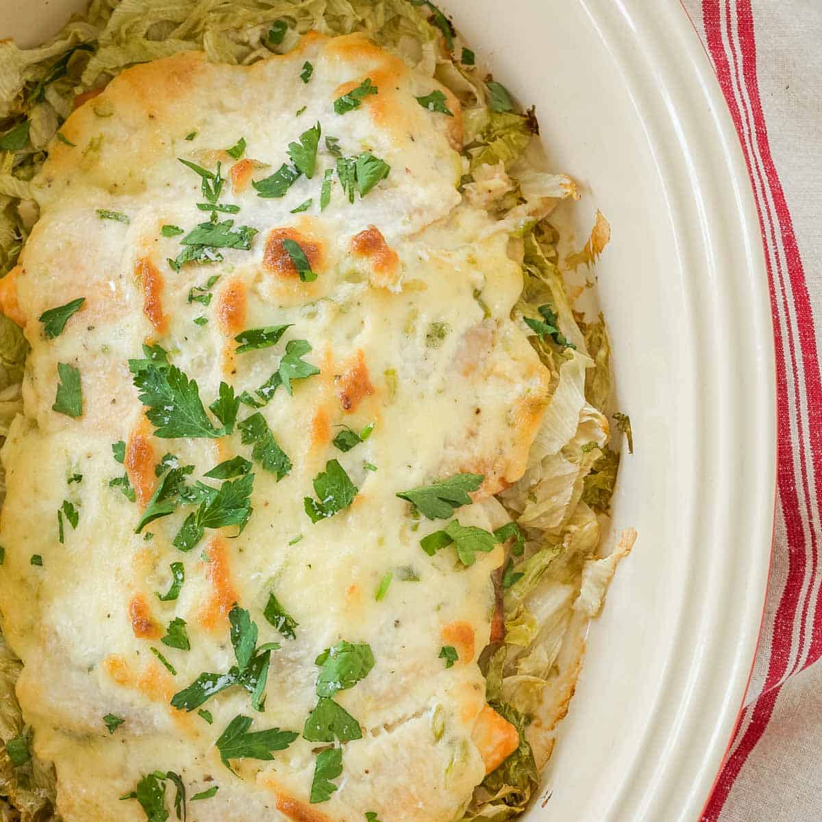 Overhead of white dish holding Baked Fish topped with a mayo sauce and sitting on shredded lettuce.